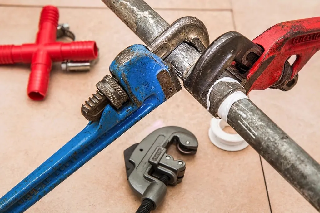 Red and blue pipe wrenches and a pipe cutter gripping a steel pipe